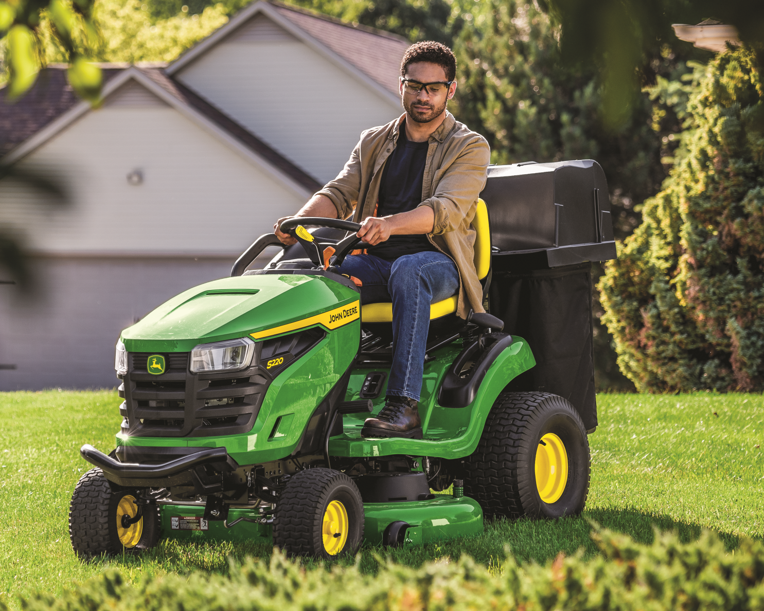 A worker is riding on a John Deere S220 Lawn Tractor