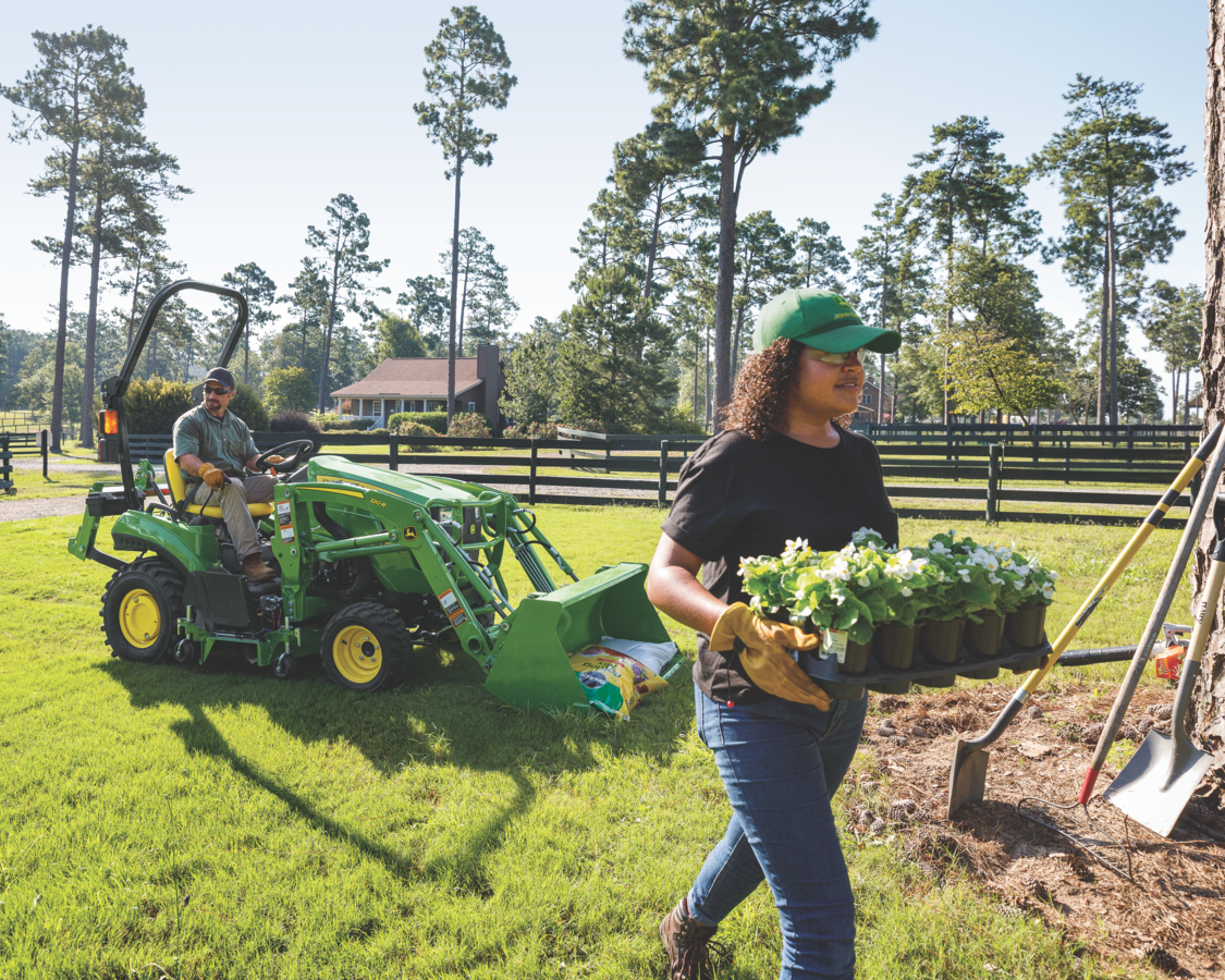 A man is driving the John Deere 1023E Compact Tractor doing gardening works