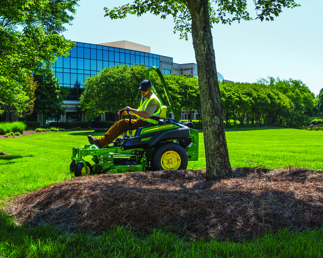 A worker is riding a John Deere Z915E ZTrak Mower to mow the lawn 